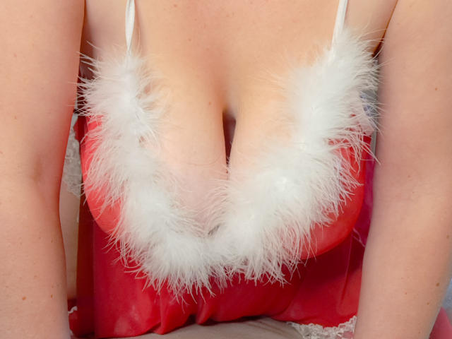 La lingerie rouge, volumineuse et duveteuse, d'EleanaRose, ornée de plumes blanches, révèle sa poitrine. Sa peau claire et ses petits mamelons roses sont visibles. Ses bras sont de chaque côté..