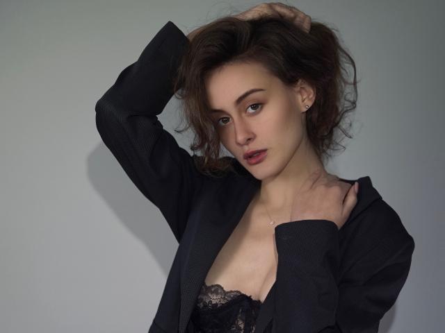 AlesyaDrons with brown hair, wearing black blazer, lace bra, and earrings, hand in hair, looking to side, soft lighting, slight shadow, subtle makeup, confident, sexy.