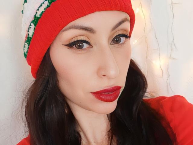 AliceRossi with red lipstick, black eyeliner, and red beanie, wearing a red top, has brown eyes, and dark wavy hair, smiling with slightly parted lips.