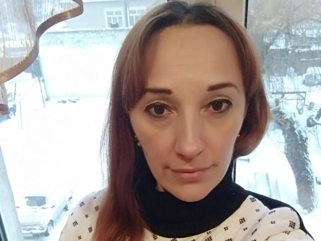 MissieLorrie has a cute face with brown eyes, straight red hair, and a black turtleneck, wearing a white shirt with black patterns, in a snowy window.