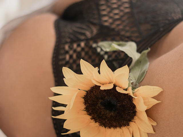 VioletaSteels Hintern in schwarzen Spitzenunterwäsche, mit einem gelben Sonnenblumenmotiv auf der Gesäßwange, wobei ihre gebräunte Haut und die floralen Spitzenakzente zur Geltung kommen..