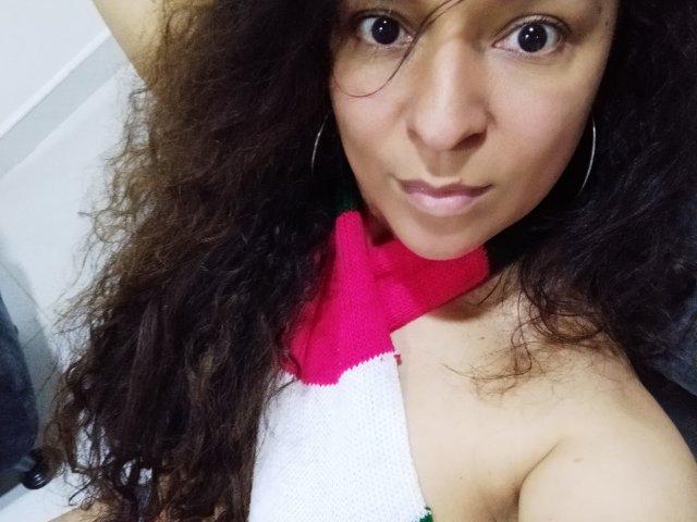 Angelonix with curly brown hair, large brown eyes, and light brown skin, wearing a white halter top with pink and green accents, showing her bare shoulders and small tits.