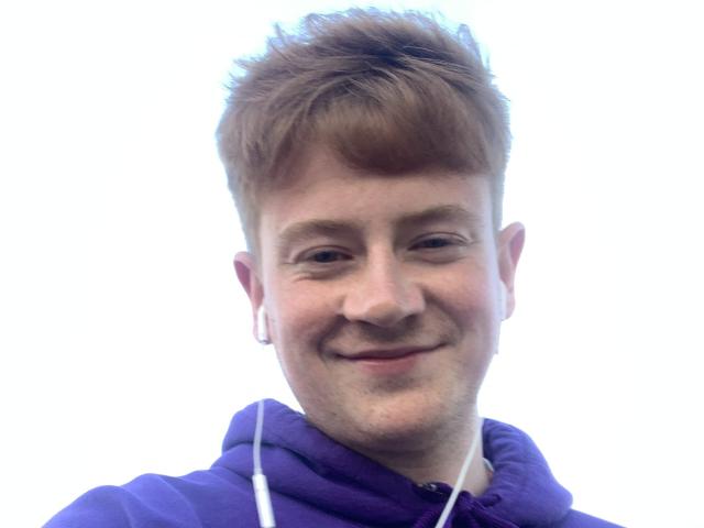 ZolotseEric tiene el cabello castaño claro y puntiagudo, una ligera sonrisa, y lleva una sudadera morada con auriculares blancos. Su rostro está ligeramente enrojecido..