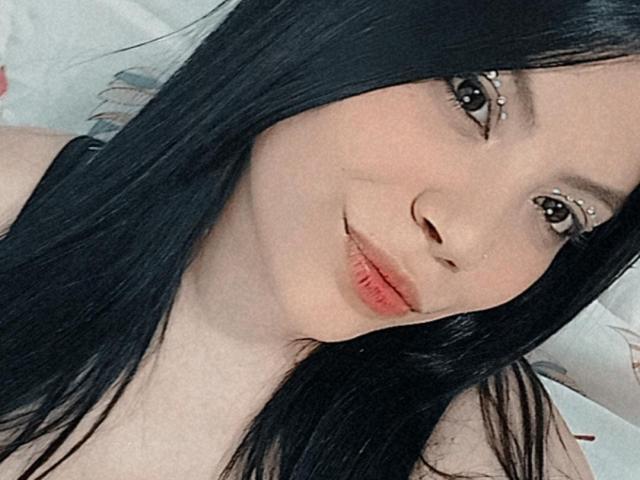 KanyaFox mit langem, schwarzem Haar, heller Haut und vollen, roten Lippen, die in die Kamera lächelt und ein dezentes Augen-Make-up trägt. Ihr Hintern ist nicht sichtbar..
