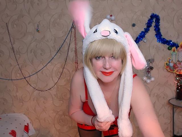 SamanthaLala with blonde bob, red lipstick, and white bunny hat, exposing her tits in red lingerie, holding hat strings, smiling at the camera.