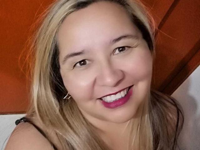 AmbarSimmons has blonde hair, brown eyes, and a smile with pink lipstick. She's wearing black earrings and has a slight tan. Her tits are not visible.