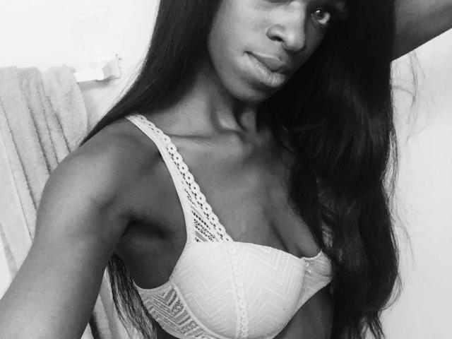 PrettyPrisca, con i suoi lunghi capelli scuri, indossa un reggiseno di pizzo bianco, mettendo in mostra il suo seno piccolo e il suo corpo snello e tonico in un selfie in bianco e nero. Sta guardando la fotocamera..