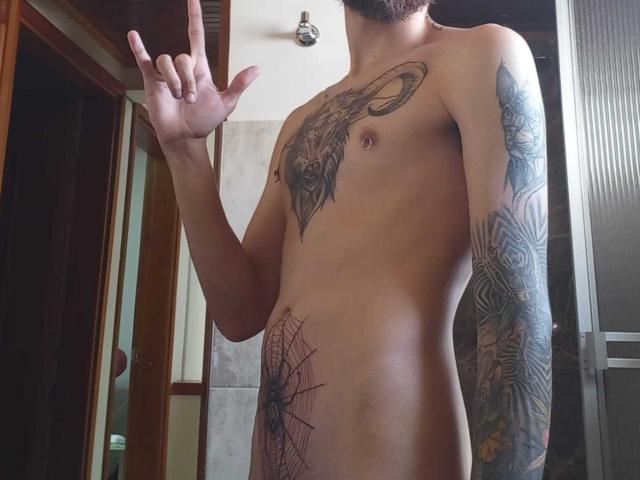 AndersX es un hombre sin camisa, con tatuajes, que levanta el dedo medio, mostrando un tatuaje de un carnero en el pecho, un tatuaje de telaraña en el abdomen y tatuajes en los brazos..