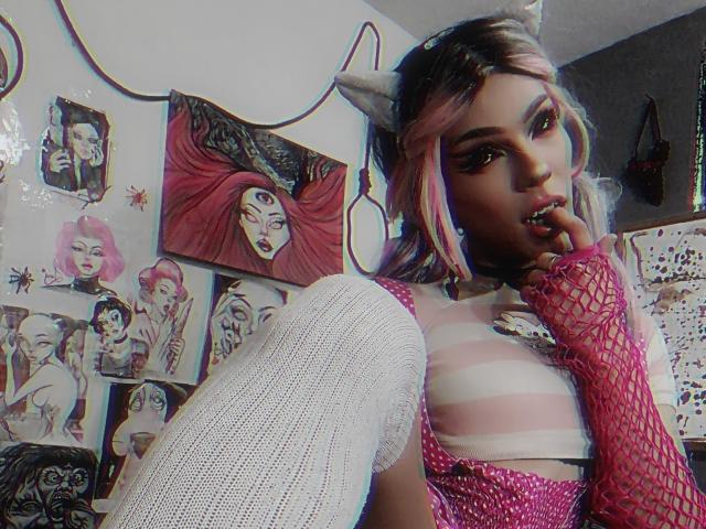 LucyVendeta con cabello rosa y azul, diadema con forma de cuerno, manga de red en el brazo, top a rayas, calcetines blancos hasta la rodilla, dedo en la boca, sujetador rosa con púas, maquillaje morado, piel oscura, pose sensual..