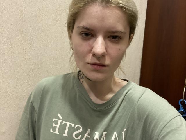 AlexSantorski ha una carnagione chiara, capelli biondi chiari e un'espressione neutra. Indossa una maglietta verde con scritte bianche e ha un piccolo tatuaggio sotto il mento..