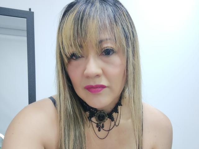 Christin Moore mit blonden und schwarzen Haaren, rosa Lippenstift, einem schwarzen Spitzen-Choker und kleinen Brüsten, die in die Kamera schaut, mit leicht geöffneten Lippen..