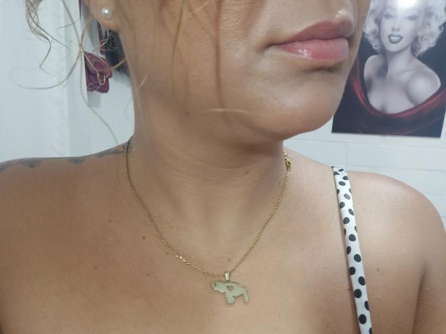 SolmaryHot's face and upper chest, showing glossy pink lips, a gold elephant necklace, and a polka-dotted strap, with a tattoo visible on the left shoulder.