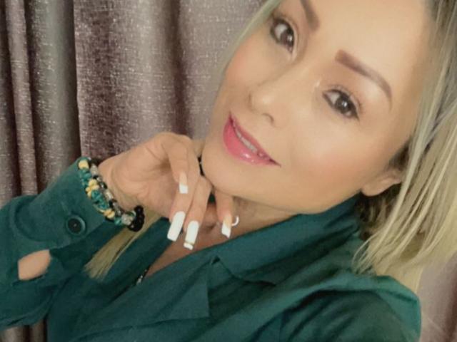 Holly Madison tiene cabello rubio, lápiz labial rosa, uñas blancas y lleva una camisa verde con pulseras de cuentas, sonriendo a la cámara..