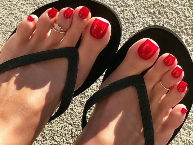 BelleLisaG's feet with shiny red nail polish, wearing black flip-flops, has a silver ring on the big toe of her right foot, and another on her left toe.
