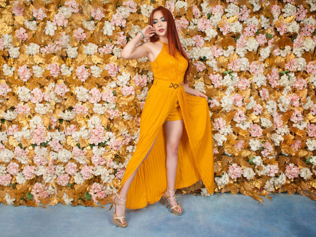 VictoriaGusman with long red hair, yellow dress, high slit, gold belt, standing, hand on hip, gold high heels, floral wall, confident pose, sexy, full body, colorful background.