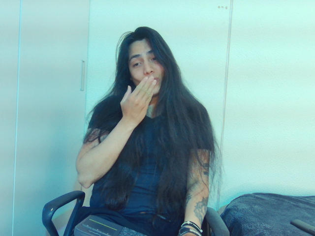 Una persona llamada Igorendon, con cabello negro largo, camisa negra y tatuajes, cubriéndose la boca con la mano, sentada en una silla, usando pulseras, mirando a la cámara, en una foto ligeramente borrosa con tonos azules..
