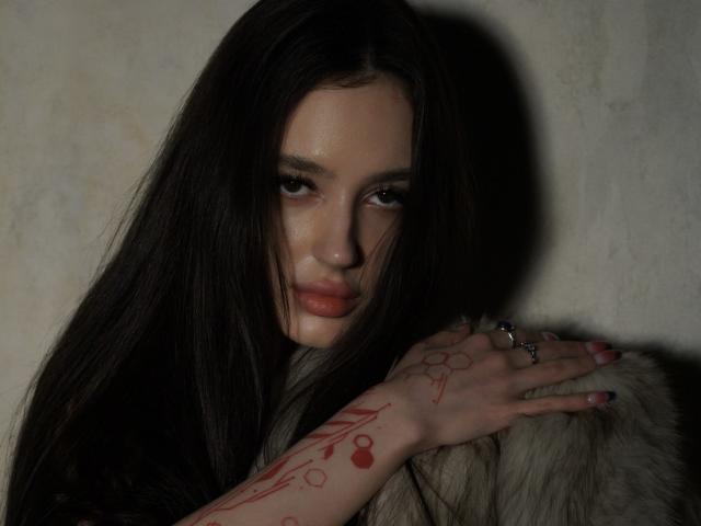 Deviline, com longos cabelos pretos, tatuagens vermelhas no braço, segurando uma pele de animal, com um olhar sedutor, olhos escuros, lábios vermelhos, usando anéis, luz sombria, olhar intenso, sexy..