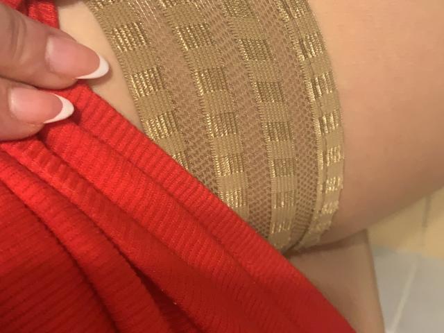 QueenKaly's hand with French-manicured nails pulls up a red ribbed garment, exposing gold mesh fabric covering her butt.