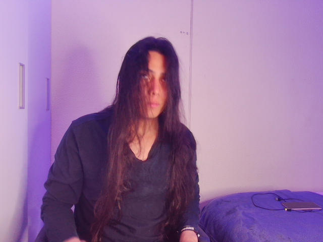 Una persona llamada Igorendon, con cabello largo y oscuro, vistiendo una camisa negra, sentada con el rostro ligeramente borroso, un cojín azul en el fondo, y un teléfono inteligente a la derecha..