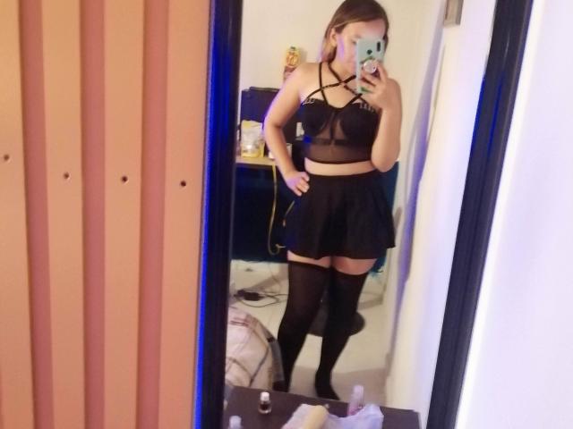 TamyParist in un selfie allo specchio, indossa un reggiseno nero con spalline sottili, una gonna nera e collant alti fino alla coscia, con il telefono che le copre il viso, mostrando i suoi seni e i suoi glutei..