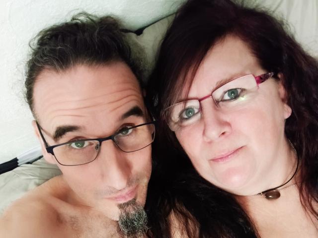 InstantShow69 avec des lunettes, des cheveux bruns et une petite barbe, et InstantShow69 avec des lunettes rouges, des cheveux foncés et un collier, allongés côte à côte, tous deux avec une peau claire et de légers sourires..