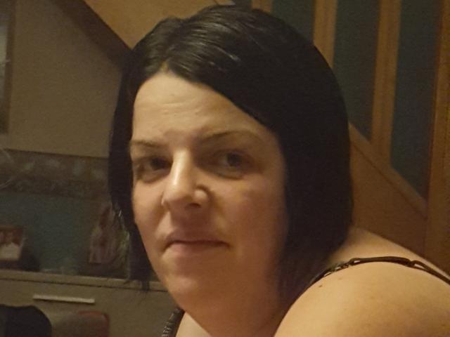 MimiSammy mit kurzen, schwarzen Haaren, leicht zusammengekniffenen Augen und einem leichten Lächeln, die ihre nackten Schultern und einen Hauch eines Trägchens zeigt. Ihre Nase ist klein und leicht nach oben gebogen..