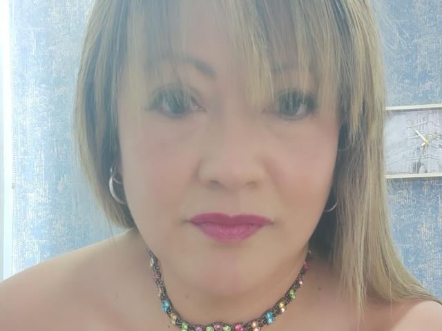 ChristinMoore has blonde hair, pink lipstick, hoop earrings, and a colorful bead necklace. She's smiling with a slight nose up, showing her bare shoulders.