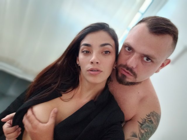HannaAndHarri, with dark hair and no makeup, has her tits exposed by Harri, who's shirtless and tattooed, with a beard, in a semi-erotic selfie.