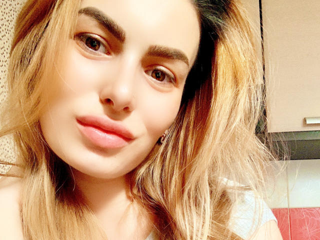 CarolRose a les cheveux bruns clairs, les yeux marron et les lèvres roses avec un léger sourire. Elle porte un haut gris et regarde l'appareil photo avec une expression détendue..