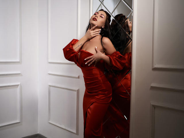 NinaTender with big tits in a shiny red dress, hand on neck, hand on boobs, mirror reflection, dark hair, closed eyes, sexy, white walls, door, sensual pose.