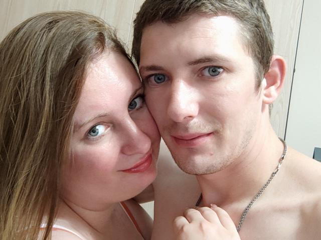 JenAndPeter, een lief koppel, waarbij Jen's borsten tegen Peter's schouder gedrukt zijn, beiden glimlachen, Jen's bruine haar, Peter's blauwe ogen, kort bruin haar, een ketting, Jen's roze top, Peter zonder shirt..