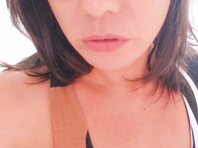 Das Gesicht von MeahBrunette mit rosafarbenen Lippen, einer kleinen Nase und braunen, schulterlangen Haaren. Sie trägt ein schwarz-weißes Oberteil, das ihre nackten Schultern und ihr Dekolleté zeigt..