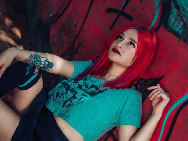CameroonSweet with red hair, green tee, black knee socks, and tattoo on right arm, lying down, looking up, showing her tits and pussy under her tee, in graffiti setting.