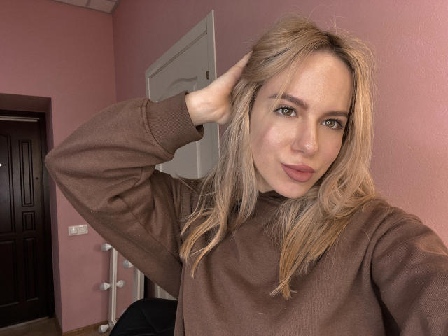 CandyWithBrandy, loira, vestindo um suéter marrom, mão no cabelo, lábios curvados, olhos verdes, parede rosa, porta, porta marrom escura, tomada de parede branca, selfie casual, fofa, atraente..