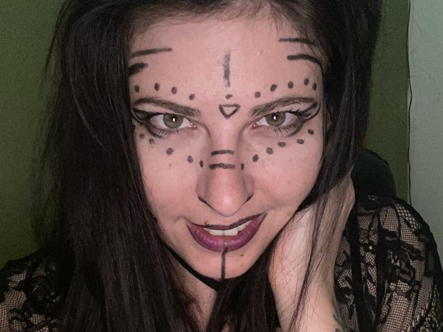 DagmarEtMirana with black dot face paint, brown eyes, purple lipstick, black lace top, and dark hair, hand on cheek, looking at camera. Boobless, assless, pussyless, focused expression.