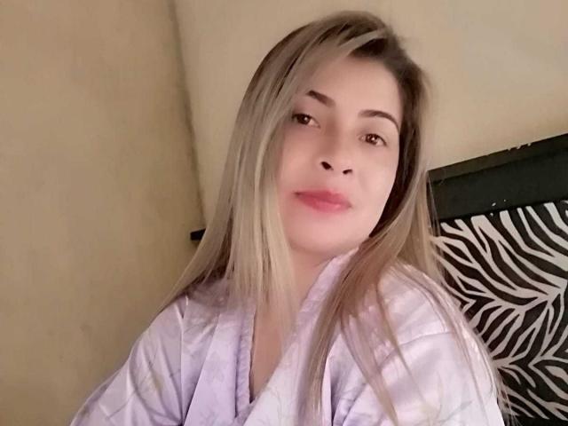 BrendaJess ha i capelli castano chiaro, le labbra rosa e indossa un kimono bianco. Ha il seno piccolo ed è seduta contro una sedia con motivo a zebra..