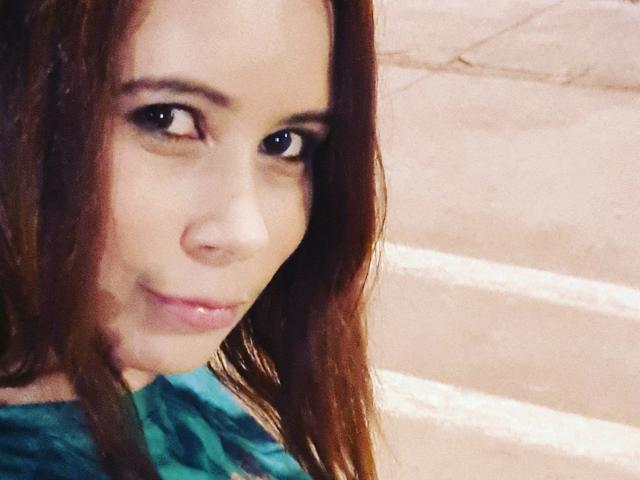Il viso di GiovannaSweet, con i capelli castani, gli occhi scuri e un leggero sorriso, indossa una maglietta verde, in un selfie sfocato. Il suo naso è piccolo e le labbra sono lucide..