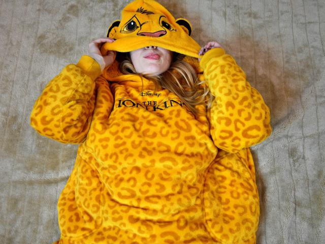 MeganCandy è sdraiata su un letto, indossando una tuta gialla con stampe di leopardo e un cappello abbinato, con il viso parzialmente coperto, e i capelli biondi visibili, appare carina..