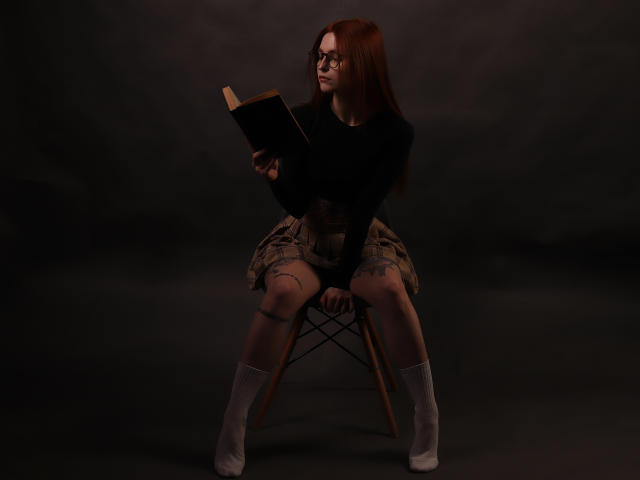 Malena, cheveux roux, lunettes, pull noir, jupe à carreaux, chaussettes blanches et chaussures blanches, assise sur une chaise, tenant un livre, fond sombre, expression concentrée, regardant sur le côté..