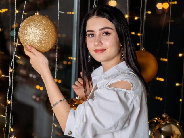 Sofia: Cabelos pretos lisos, segurando uma esfera dourada brilhante, vestindo uma camisa branca com recortes, brincos de prata e um bracelete, sorrindo suavemente para a câmera..
