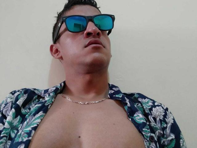 Vergara with a chubby, fair-skinned face, short dark hair, wearing blue-green sunglasses, and an open floral shirt, showing a chest necklace. Vergara's face is slightly tilted upward.