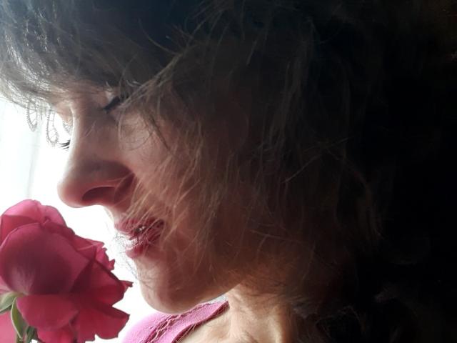 Le visage d'Orshiti en profil, avec ses cheveux bruns en désordre, tenant une rose rouge près de sa bouche, ses lèvres légèrement entrouvertes. La lumière du soleil illumine son nez et sa joue..