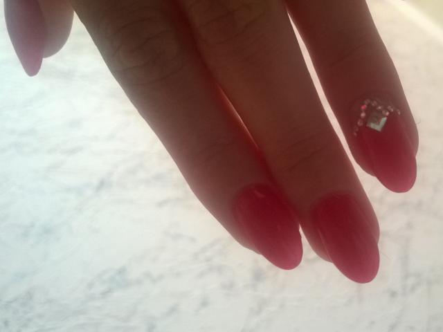 AnabelSex69's fingers with shiny red nail polish, one nail has a small pink gem and clear square stone, in a slightly blurred image.