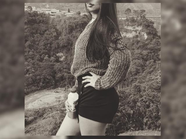 SteffanyTaylor with long hair, wearing a knitted sweater and black shorts, holding a cup, standing sideways, showing her ass and hand on hip, in a black-and-white photo.