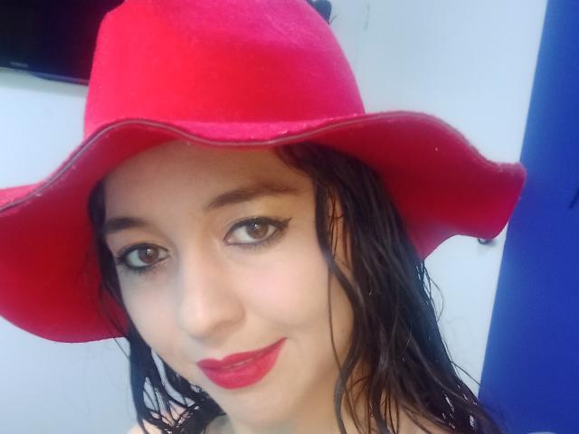 NalimiSmirnov mit nassen, schwarzen Haaren, die einen leuchtend roten Hut und roten Lippenstift trägt, lächelt in die Kamera und zeigt ihr süßes Gesicht und ihre attraktiven braunen Augen..