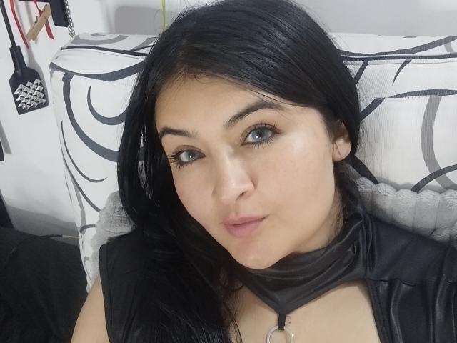 LindaSophieX has black hair, green eyes, and is wearing a black leather choker with a ring, looking at the camera with a slight pout.