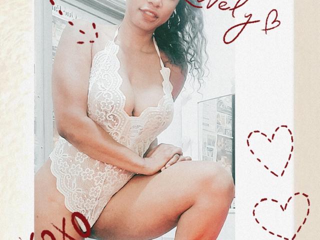 AnaSexy with curly hair, wearing a white lace lingerie bodysuit, showing her big boobs and curvy ass, squatting, smiling slightly, with hearts and "Chek" scribble in the corner.
