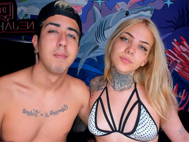 Un homme musclé et sexy, avec des tatouages, une casquette noire et un tatouage sur la poitrine, est à côté d'une jeune femme blonde, également musclée et sexy, portant un bikini noir et blanc à pois avec de fines bretelles, et les deux sourient..