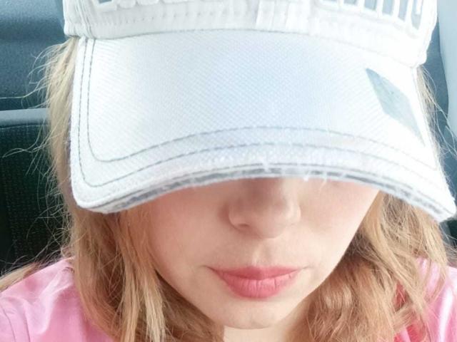 Seher's face is partially hidden by a white cap, showing her pink lips and light blonde hair. She wears a pink shirt. Her ass is not visible.
