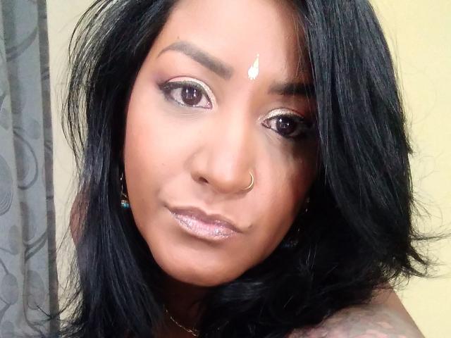 Nahirr has dark black hair, brown skin, and a small nose ring. She has shiny pink eyes, a white forehead dot, and sparkly pink lips. Nahirr's face is centered.